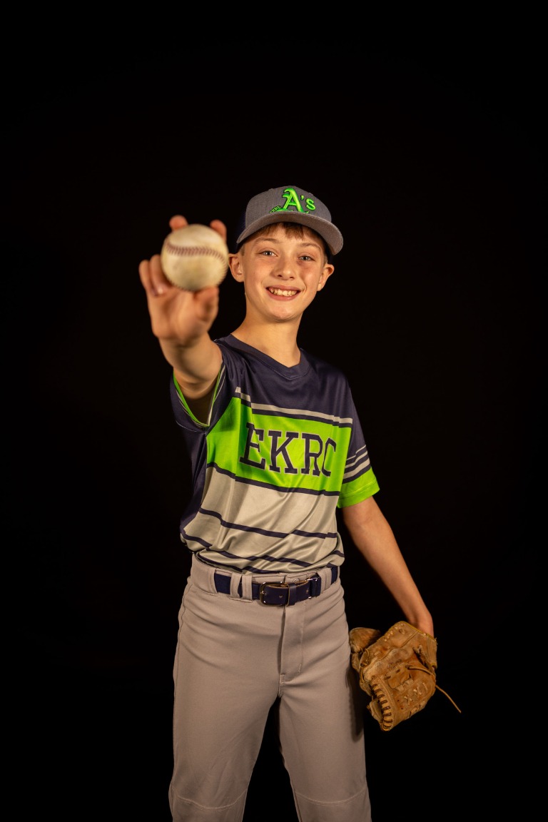 A young baseball player holding out a baseball