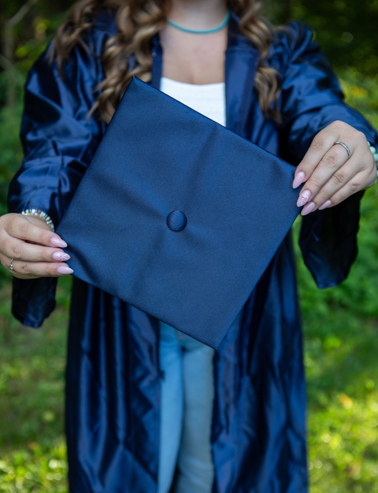 A graduate holding her cap among the trees