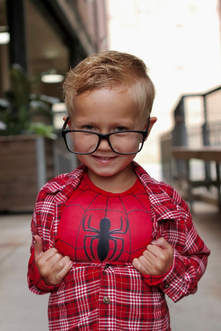 A little superhero smiling in glasses and a red costume
